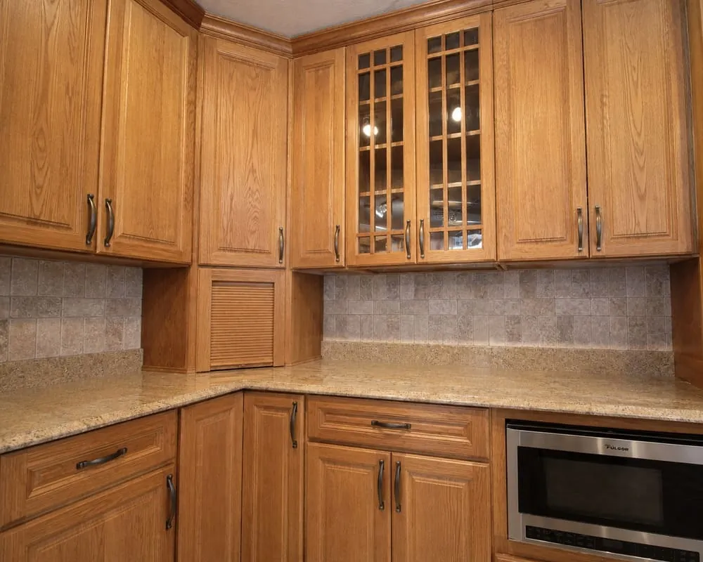 Before: kitchen with dated honey-oak stained cabinetry, glass-front uppers, and a granite worktop