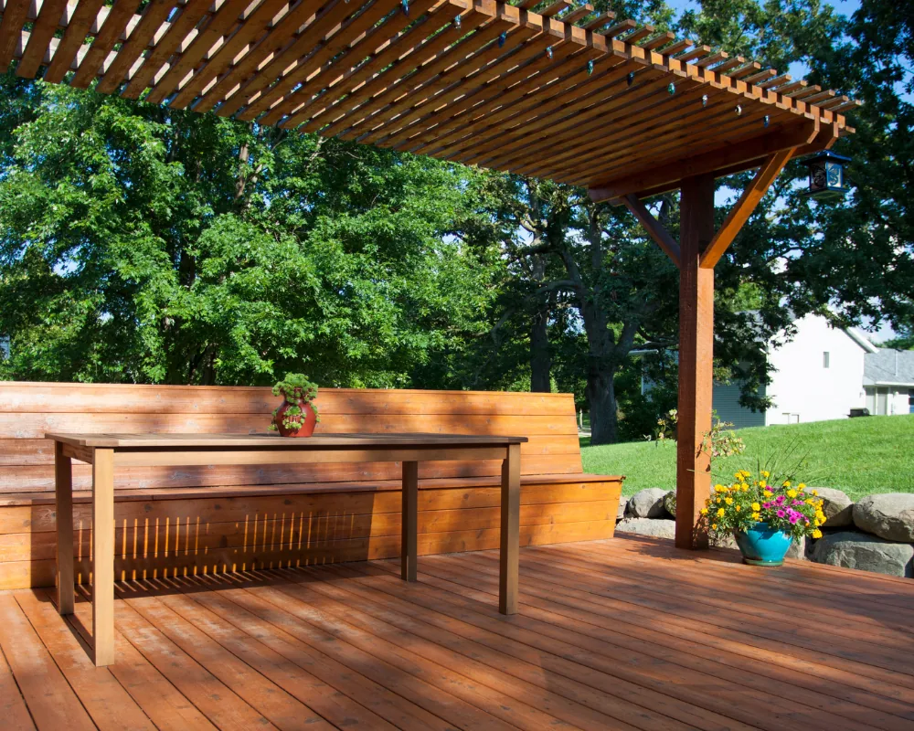 After: the same finished cedar pergola over a stained deck with a built-in bench, dining table, and potted plants