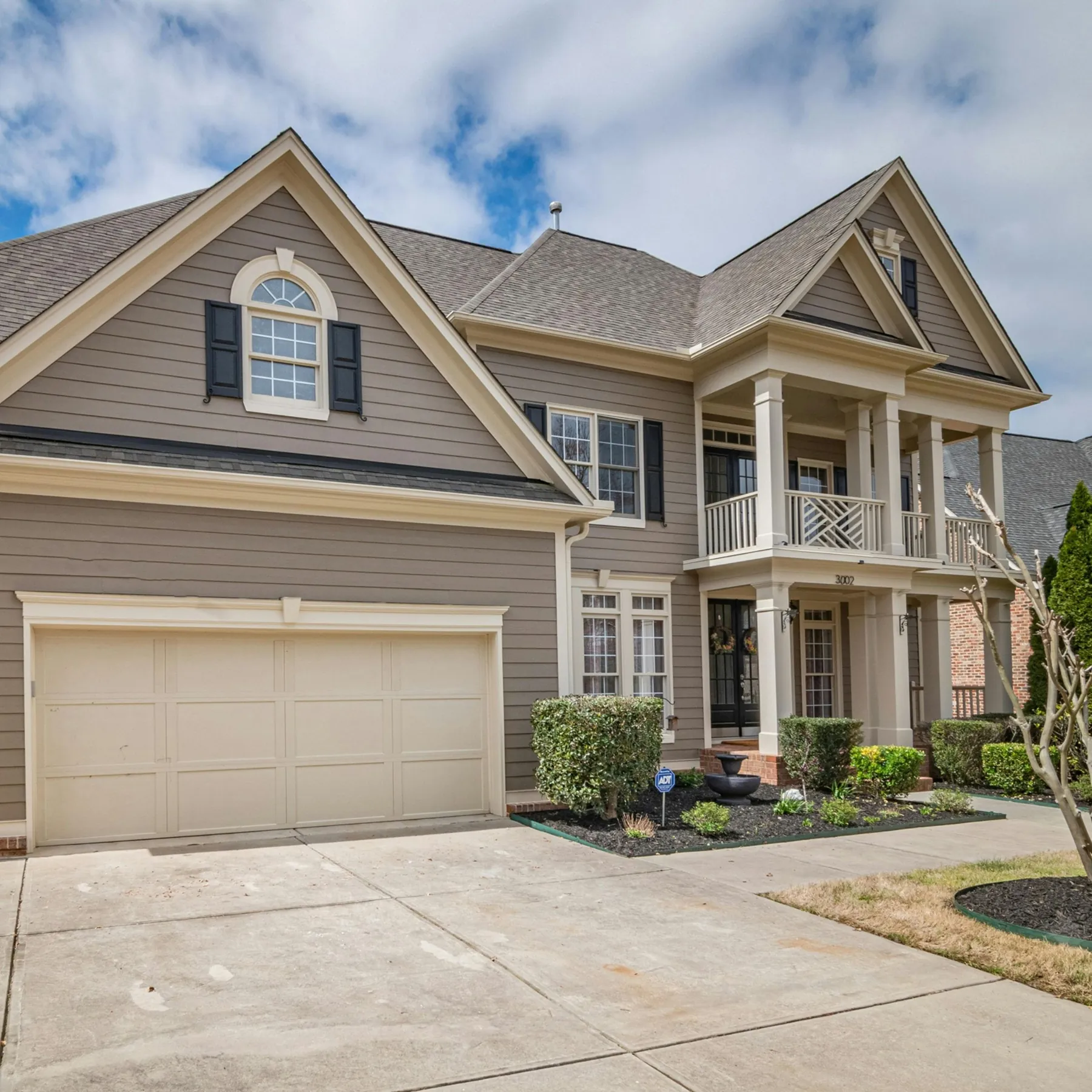 Two-storey home in warm beige with white trim and a wraparound covered porch