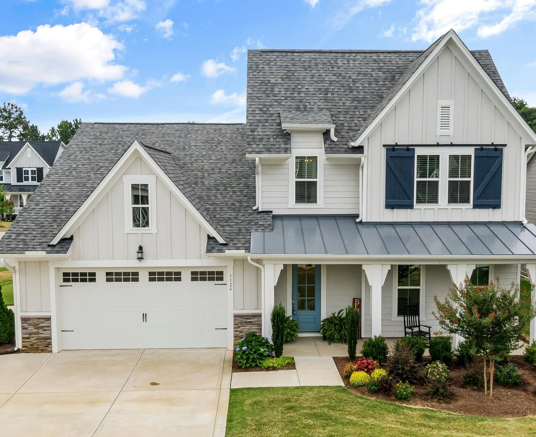 White farmhouse exterior with navy shutters, a standing-seam porch roof, and a two-car garage