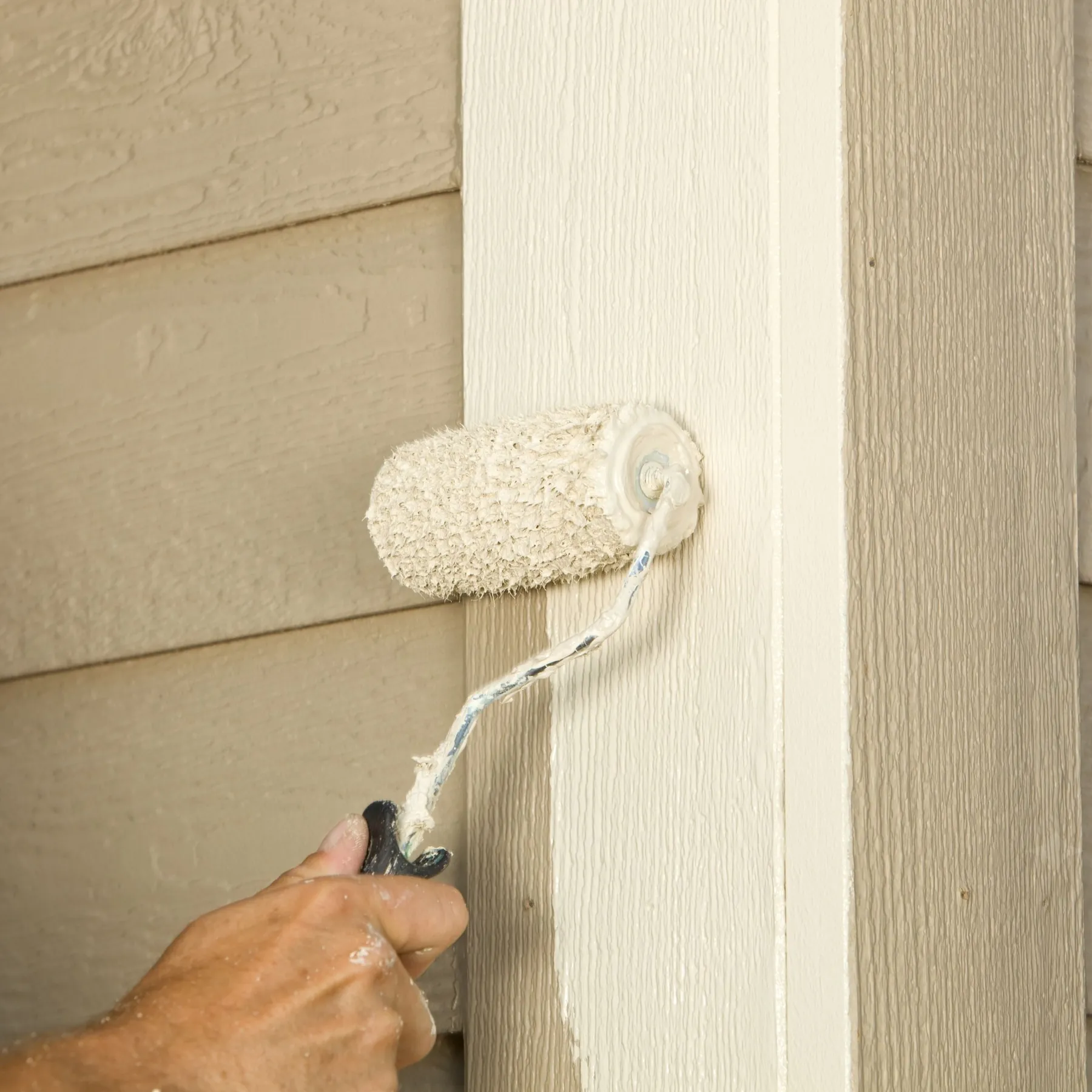 Painter rolling a fresh coat onto lap siding by hand