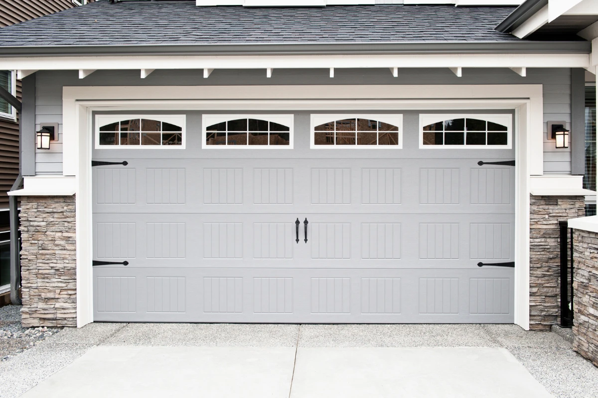 Gray carriage-style garage door with arched window panels on a stone and siding home