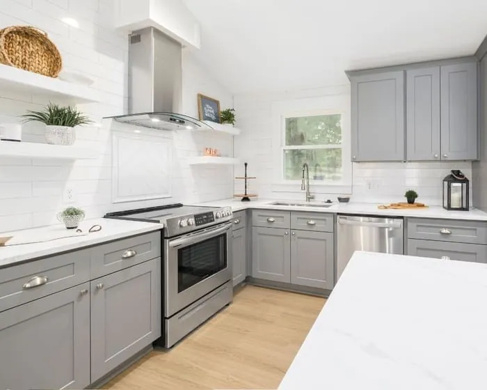 Kitchen finished in soft grey cabinetry with white worktops, a tiled splashback, and a stainless range hood