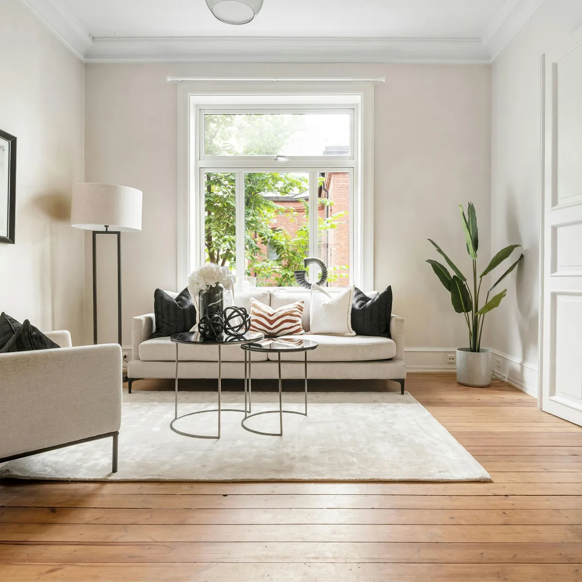 Living room painted in warm off-white, with white crown moulding, a tall sash window, and stripped timber floors
