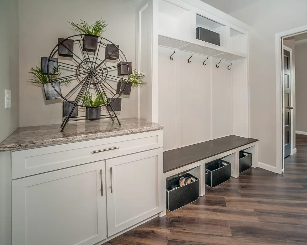 After: the same mudroom with painted white built-in lockers, open cubbies, coat hooks, and a hardwood floor