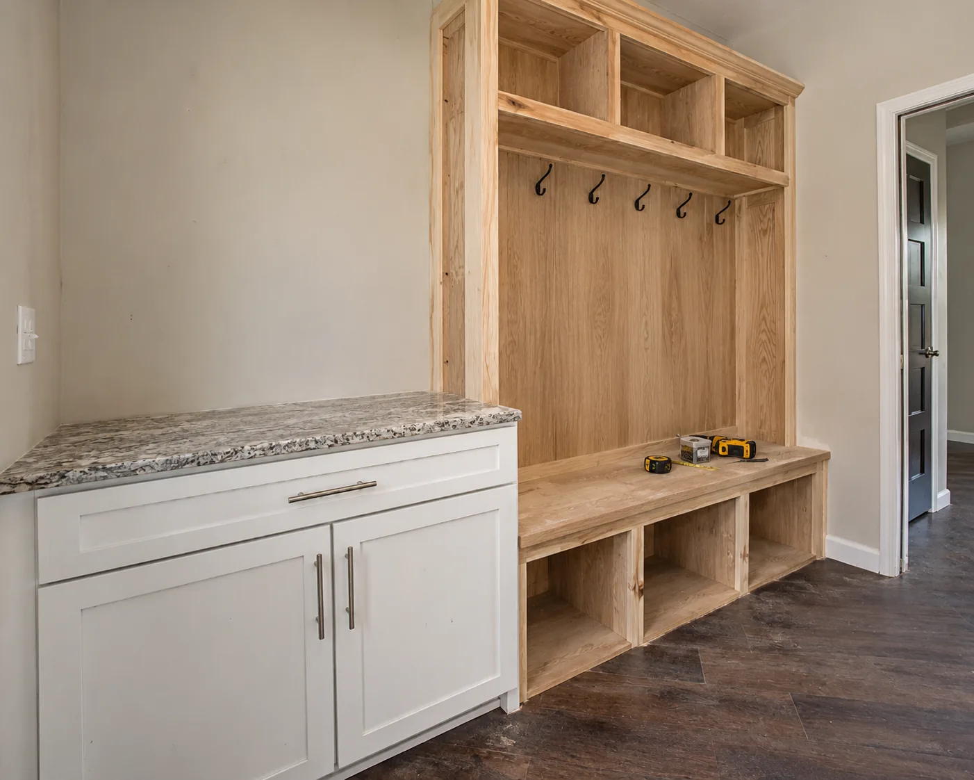 Before: mudroom nook with dated floral wallpaper, an ironing board, and unfinished MDF locker cubbies under construction