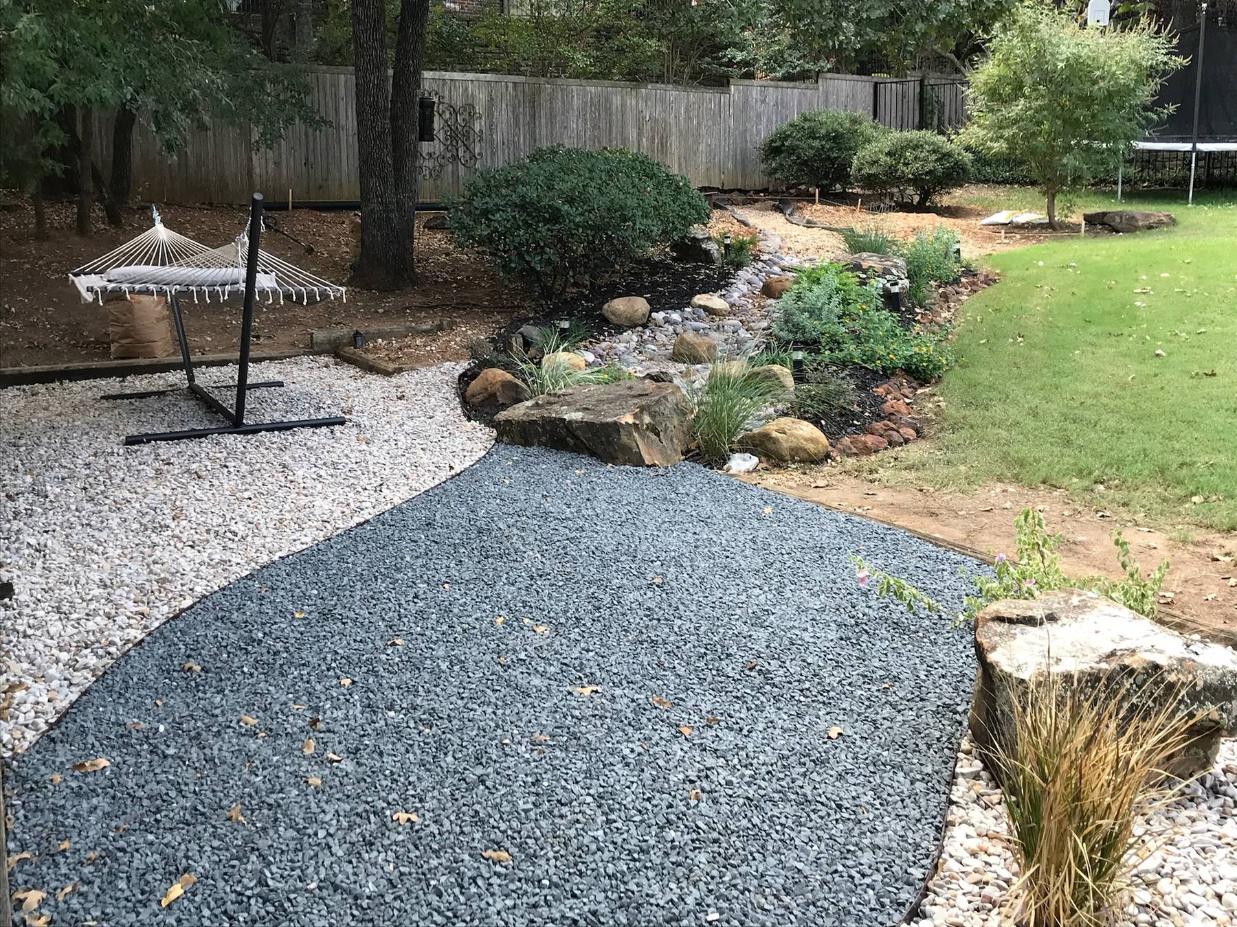 Gravel path and planted border with a hammock in a shaded garden